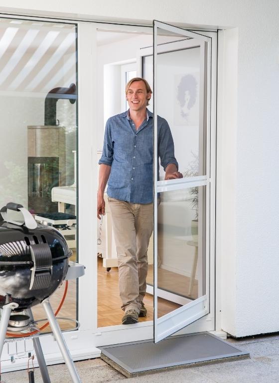 Mann tritt durch Insektenschutztür ins Haus ein